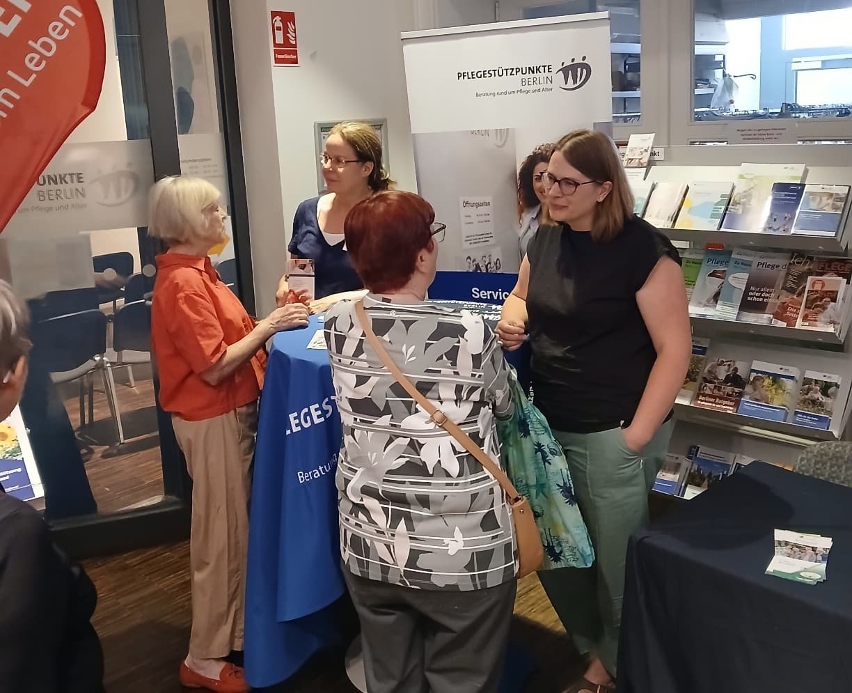 Das Bild zeigt einen Infostand auf einer Messe, auf dem mehrere Personen miteinander im Gespräch sind
